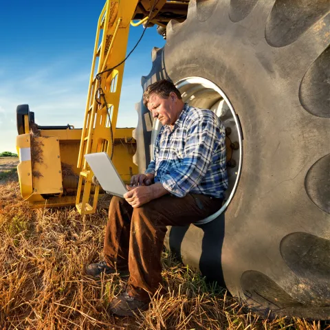 Farmer on laptop sat on tractor wheel